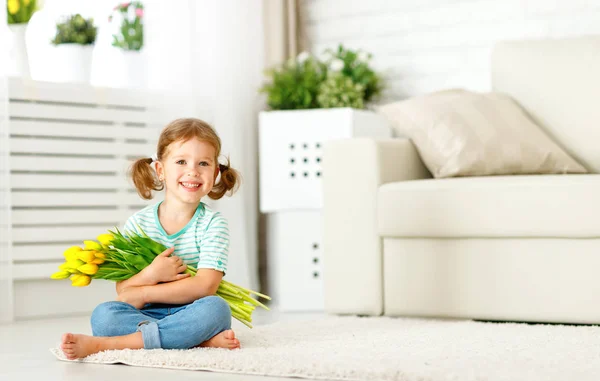 Glad skrattande barn flicka med gula tulpaner hemma — Stockfoto