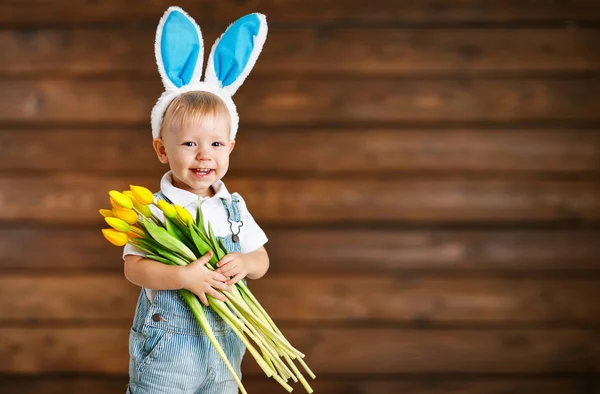 Счастливый смеющийся мальчик в кроличьих ушах с желтыми тюльпанами на голове — стоковое фото