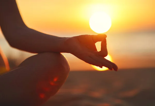 Händerna på kvinnan som mediterar i yogaställning i solnedgången på stranden — Stockfoto