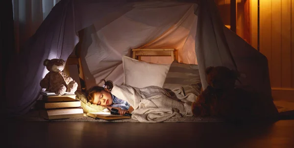 Criança menina dormindo na barraca com livro e lanterna — Fotografia de Stock