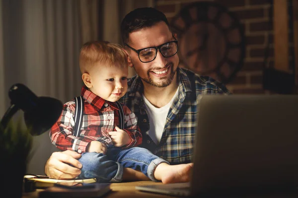 Pai e filho bebê trabalho em casa no computador no escuro — Fotografia de Stock