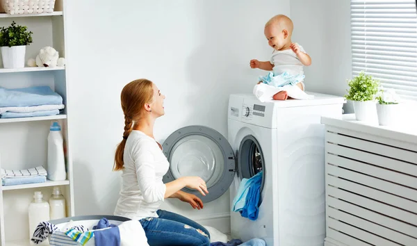 Mother housewife with baby engaged in laundry fold clothes into — Stock Photo, Image