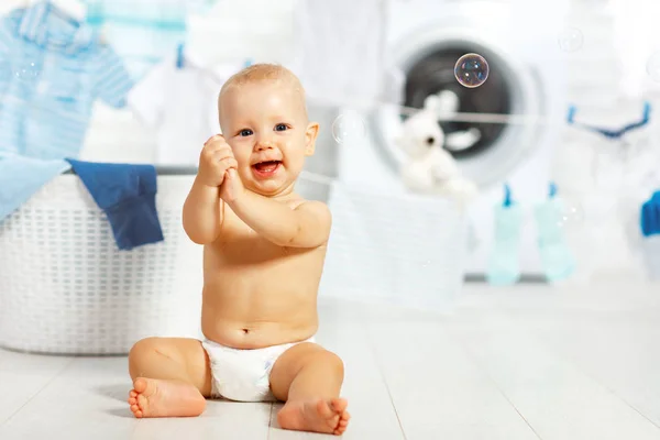 Diversão feliz bebê menino para lavar roupas e ri na lavanderia — Fotografia de Stock