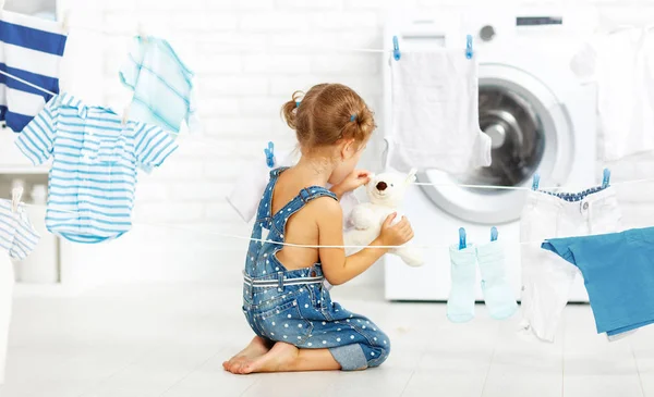 Criança divertida menina para lavar roupas e ursinho de pelúcia na lavandaria — Fotografia de Stock
