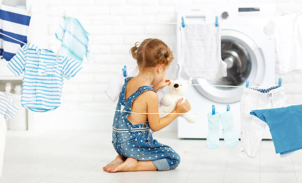 child fun little girl to wash clothes and teddy bear in laundr