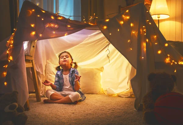Child girl playing meditates in yoga pose in tent at home — Stock Photo, Image