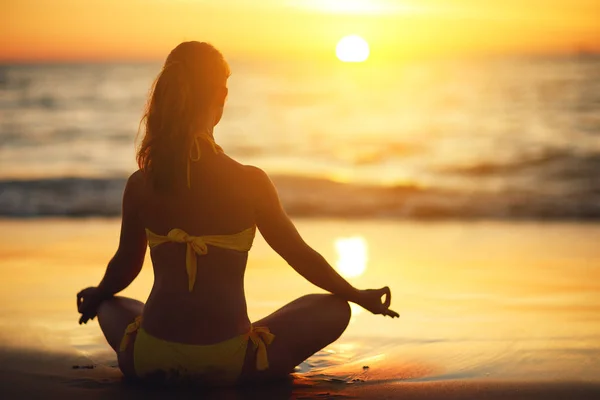 Kvinna praktiserar yoga och mediterar i lotusställning på stranden — Stockfoto