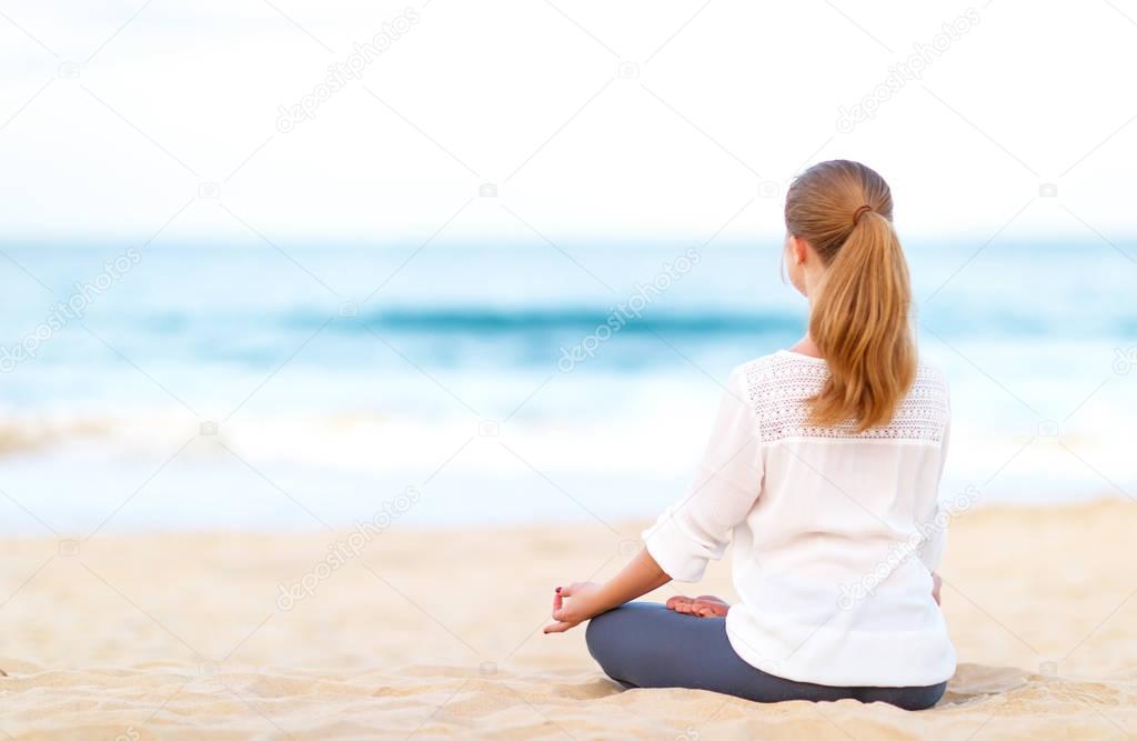 woman practices yoga and meditates in lotus position on beac