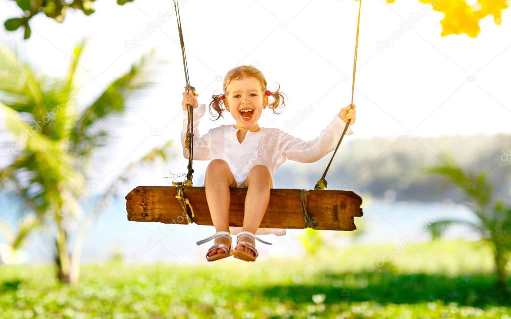 Happy child girl swinging on swing at beach  in summer