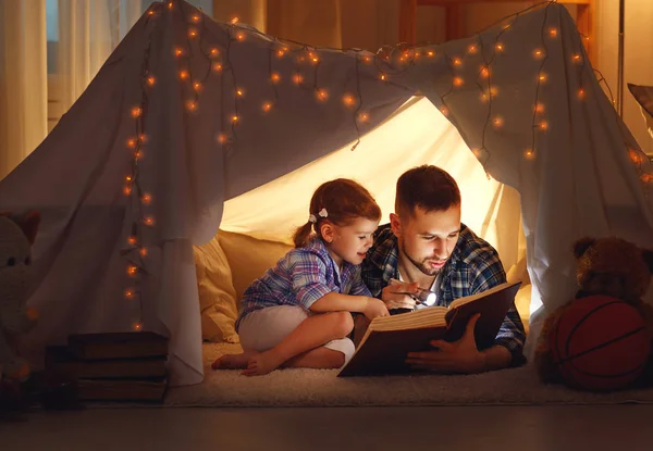 Счастливая семья отец и дочь дочь читают книгу в палатке — стоковое фото