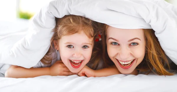 Lyckliga familjen mor och barn dotter skratta i sängen — Stockfoto