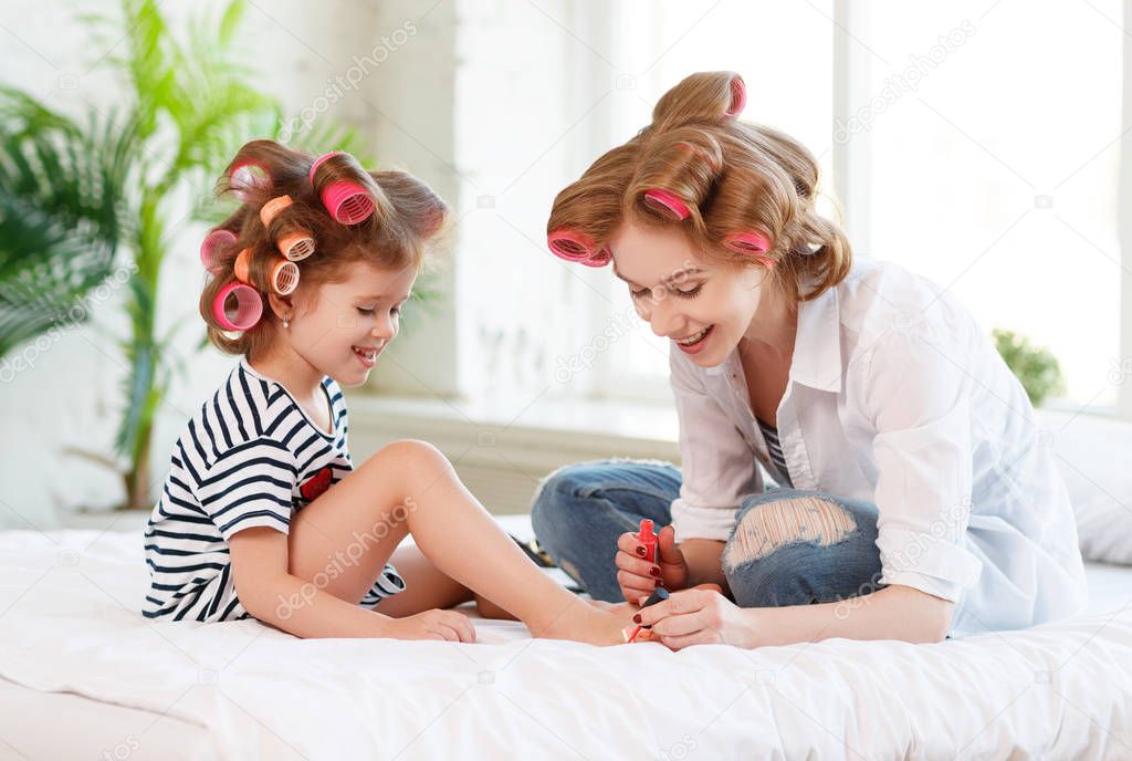 Mother and child daughter in hair curlers paint nails, make pedi