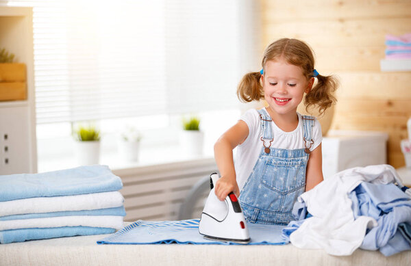 Happy   child girl ironing clothes   in laundry  