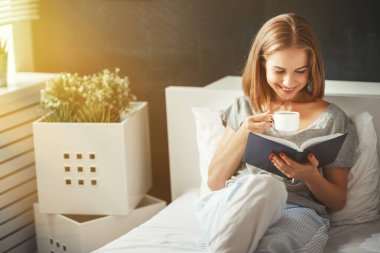 Mutlu genç kadın kitap okur ve yatakta kahve içer  