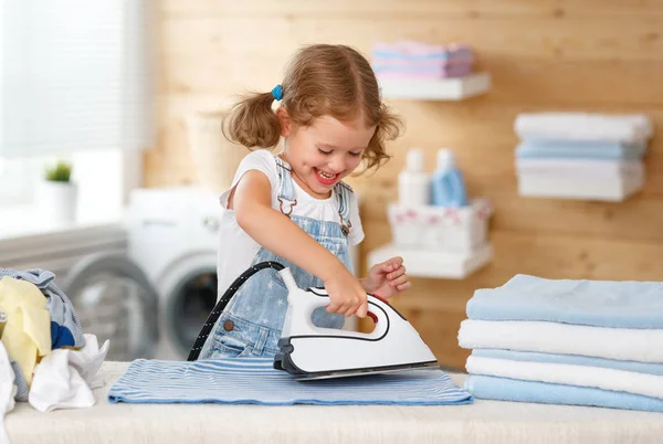 Счастливая девочка гладит одежду в прачечной — стоковое фото