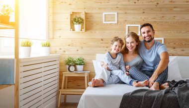 yatakta mutlu aile anne, baba ve çocuk gülüyor