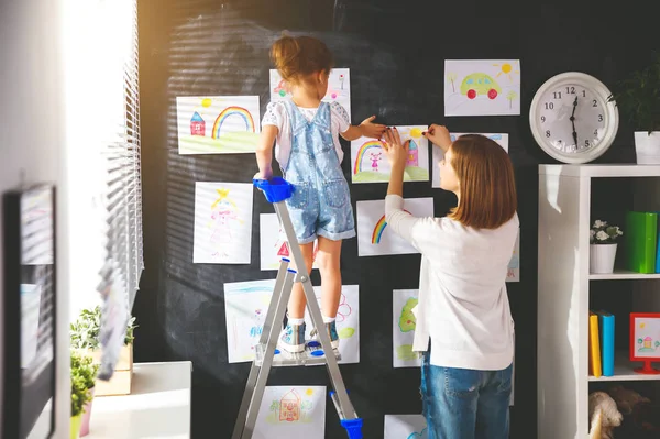 Mãe e criança menina pendurar seus desenhos na parede — Fotografia de Stock