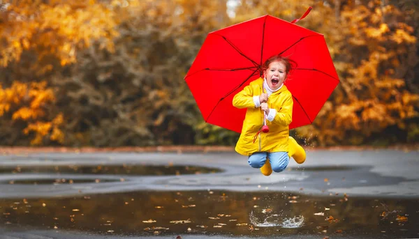 Happy child girl with an umbrella and rubber boots in puddle  on — Stock Photo, Image