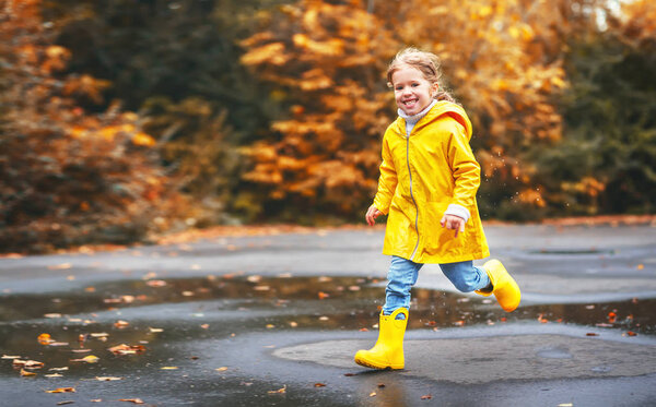 happy child girl with an umbrella and rubber boots in puddle  on