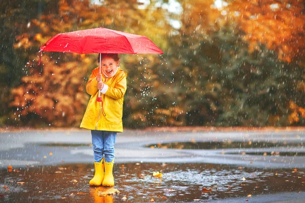 Happy child girl with an umbrella and rubber boots in puddle  on — Stock Photo, Image