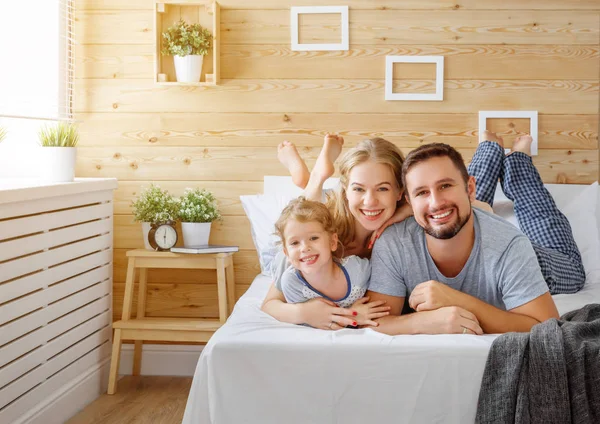 Feliz familia madre, padre e hijo ríe en la cama — Foto de Stock