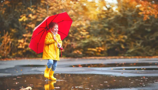 Lyckligt barn flicka med ett paraply och gummi stövlar i pöl på — Stockfoto