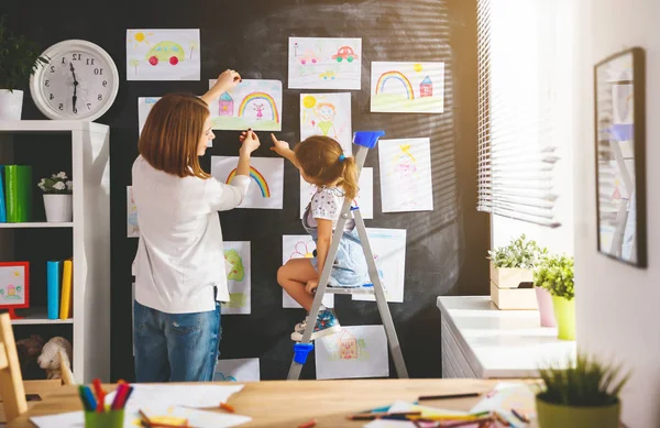 Mother and child girl hang their drawings on wall — Stock Photo, Image
