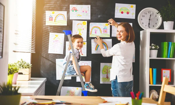 Mãe e criança menina pendurar seus desenhos na parede — Fotografia de Stock