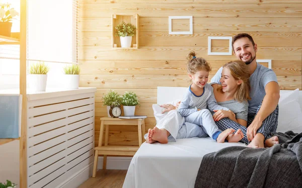 Feliz familia madre, padre e hijo ríe en la cama —  Fotos de Stock