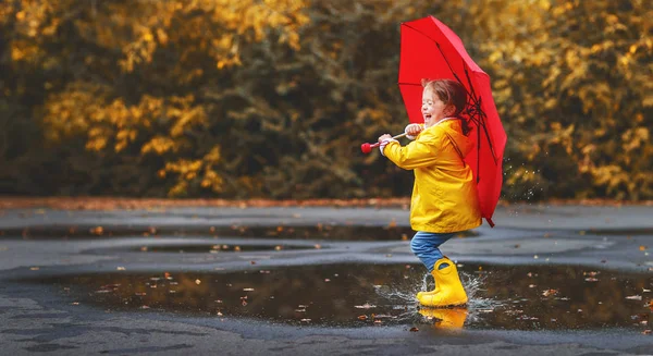 Heureux enfant fille avec un parapluie et bottes en caoutchouc dans la flaque d'eau sur — Photo