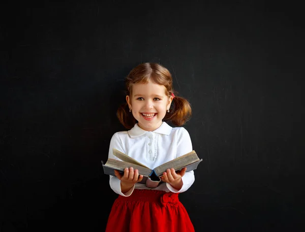 Щаслива школярка дошкільнята з книгою біля шкільної дошки — стокове фото