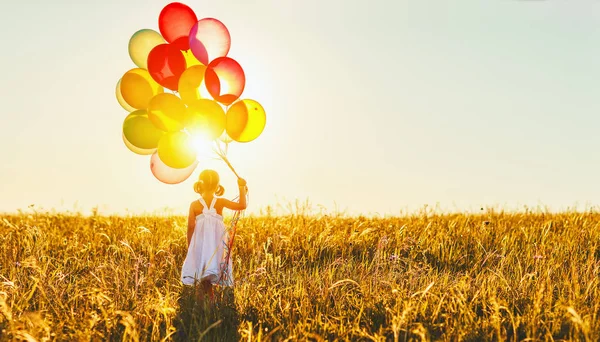 Щаслива весела дівчинка з повітряними кулями на лузі на заході сонця в с — стокове фото