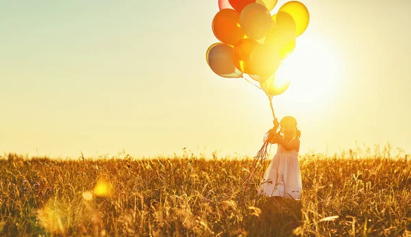 Gelukkig vrolijke kind meisje met ballonnen op de weide bij zonsondergang in s — Stockfoto