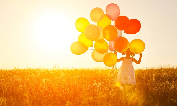 Happy cheerful child girl with balloons on meadow at sunset in s — Stock Photo, Image