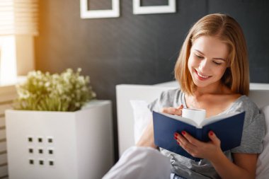 Mutlu genç kadın kitap okur ve yatakta kahve içer  