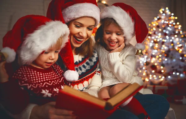 Família mãe e crianças ler um livro no Natal perto de fogo — Fotografia de Stock