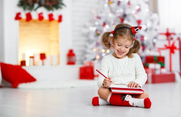 Criança menina escrevendo carta santa casa perto da árvore de Natal — Fotografia de Stock