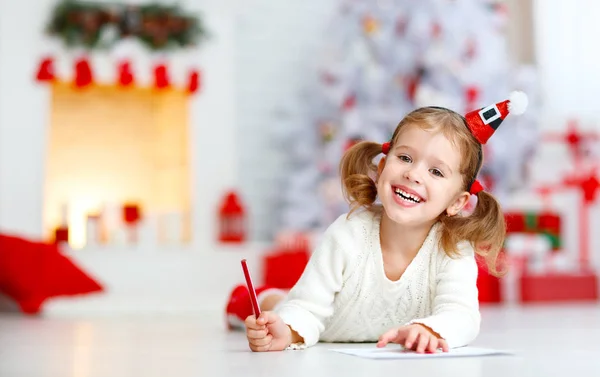 Barn tjej skriver brev santa hem nära julgran — Stockfoto
