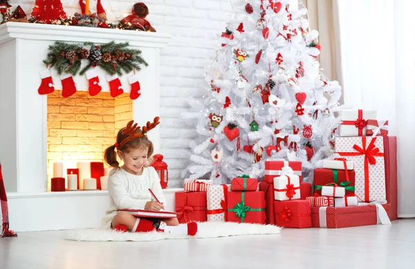 Niña escribiendo carta santa casa cerca del árbol de Navidad —  Fotos de Stock