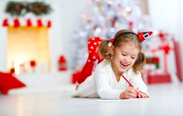 Barn tjej skriver brev santa hem nära julgran — Stockfoto