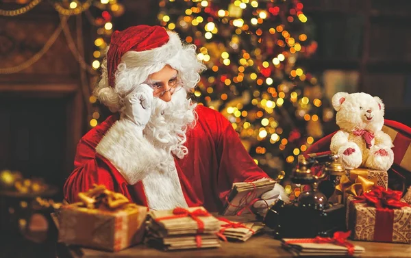 Santa Claus vid skrivbord med bokstäver och julklappar — Stockfoto