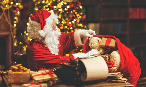 Santa Claus vid skrivbord med bokstäver och julklappar — Stockfoto