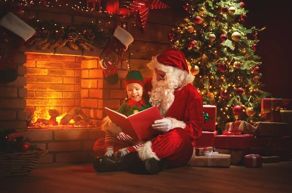 Santa claus lee un libro a un pequeño elfo por árbol de Navidad — Foto de Stock