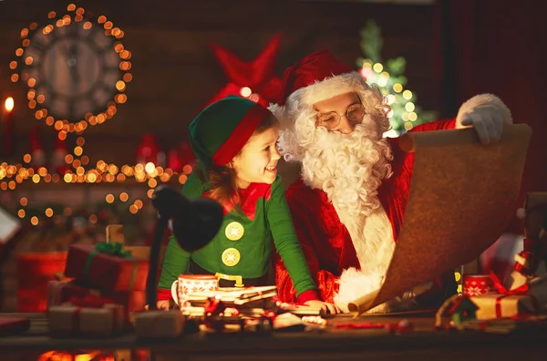 Санта Клаус читает список хороших детей маленькому эльфу на Рождество — стоковое фото