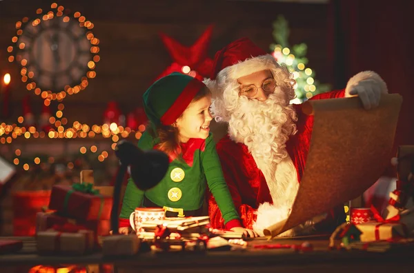 Santa claus lê lista de boas crianças para pequeno elfo por Christm — Fotografia de Stock