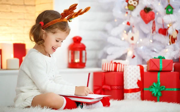 Barn tjej skriver brev santa hem nära julgran — Stockfoto