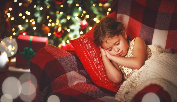 Criança menina está dormindo perto de uma árvore de Natal — Fotografia de Stock