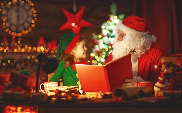Santa claus lee libro a pequeño elfo por árbol de Navidad — Foto de Stock