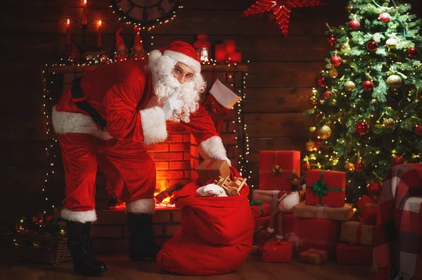 Frohe Weihnachten! Weihnachtsmann neben Kamin und Baum mit Geschenk — Stockfoto