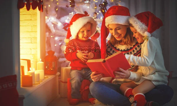 Сім'я мати і діти читають книгу на Різдво біля вогнища — стокове фото
